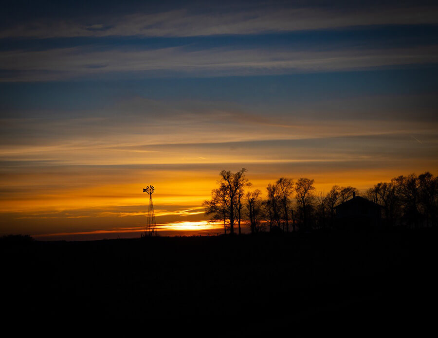 Photo taken by Colette Rathke showcasing a sunset with a windmill and trees